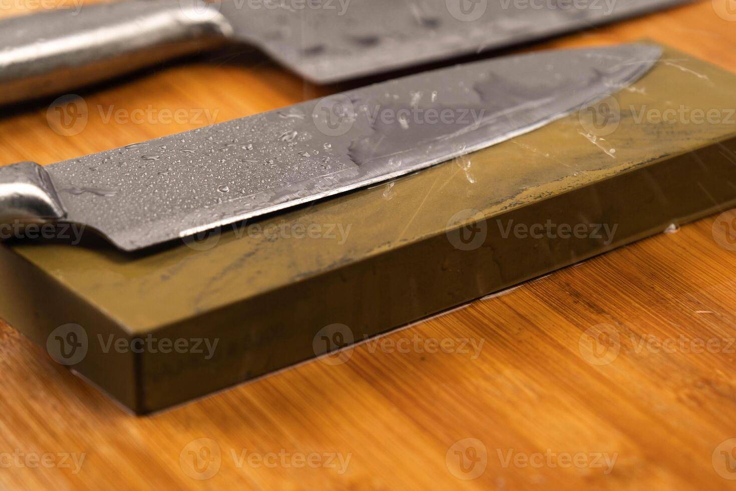 Sharpening knives with a Whetstone. Knife sharpening. Sharp knife and sharpening stone on a wooden cutting board. photo