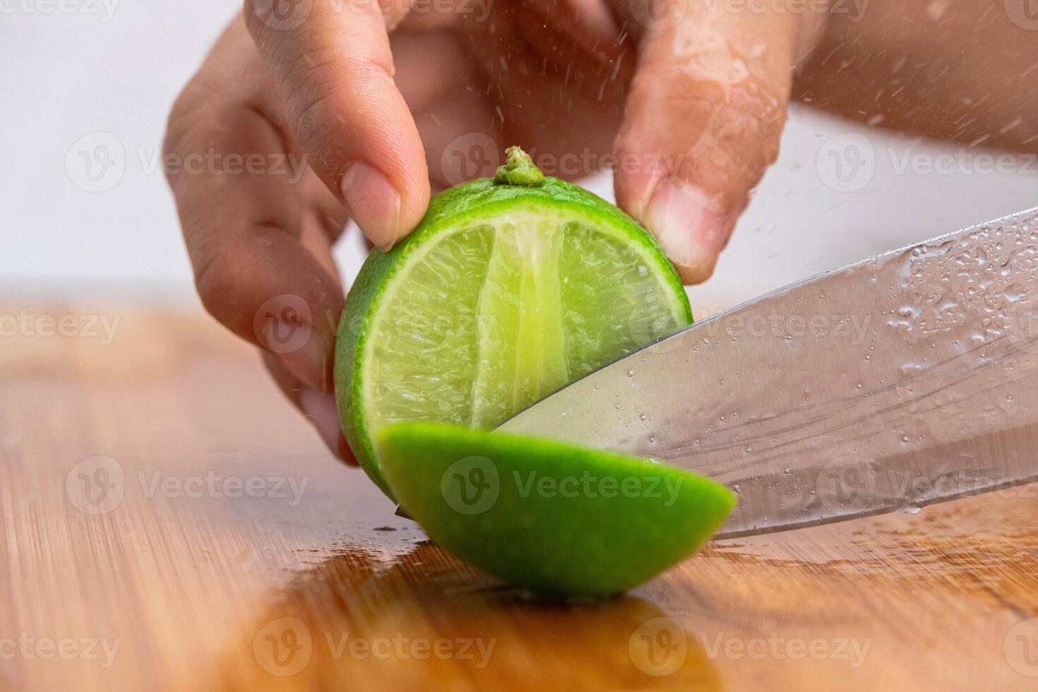 Female hand holding knife is cutting lime on a wooden board in Kitchen. Cutting fresh lemon in half close up. Hight Vitamin C Natural photo