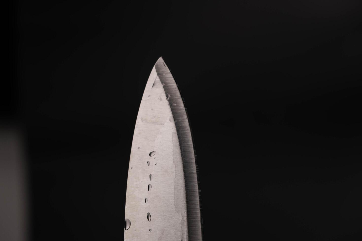 Water drop on sharp knife isolated on dark background. water splashing on knife. photo