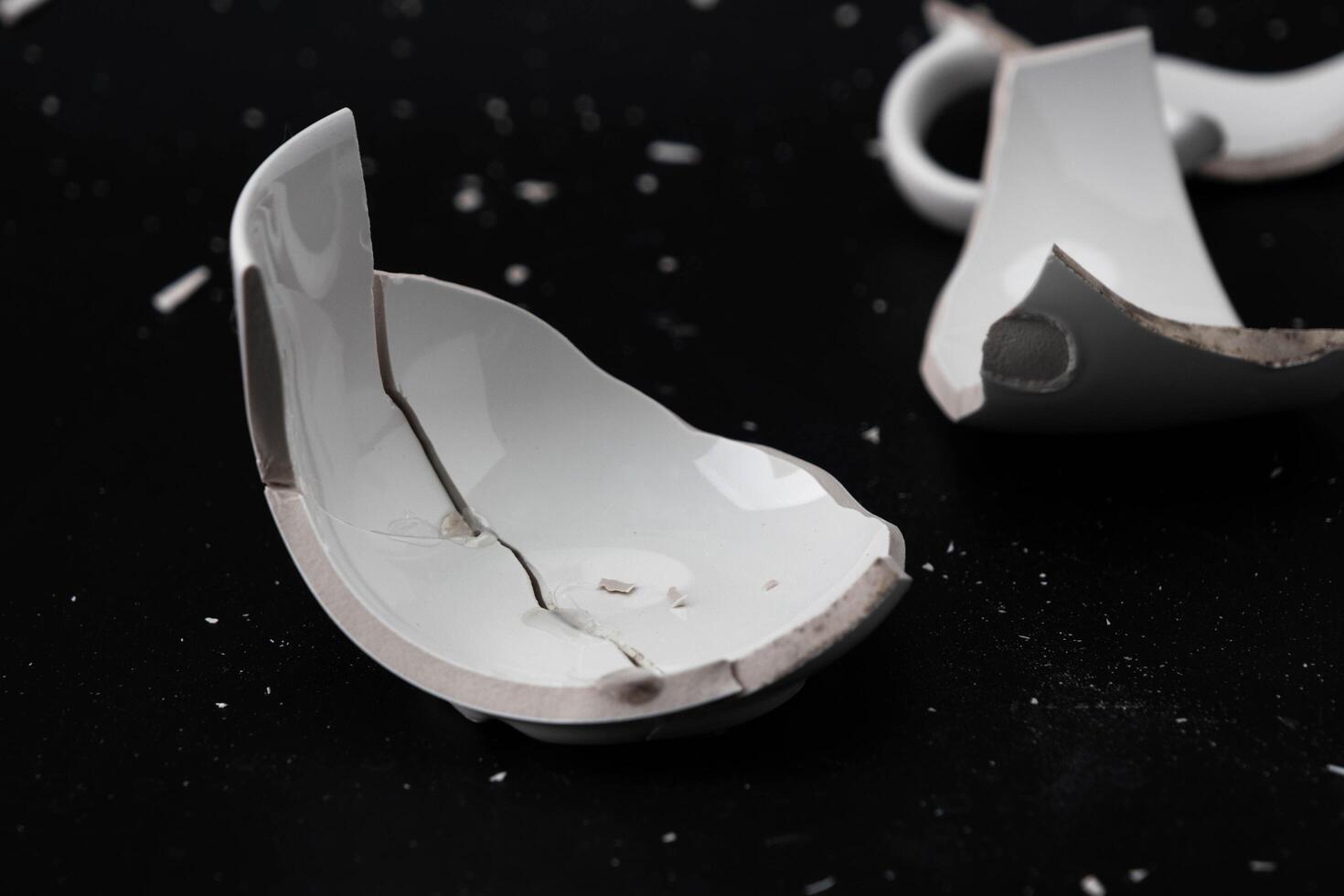 Large white mug with cracks. White cup for tea or soup with cracks isolated on dark background. Broken ceramic cup close up. symbol of divorce or loss photo