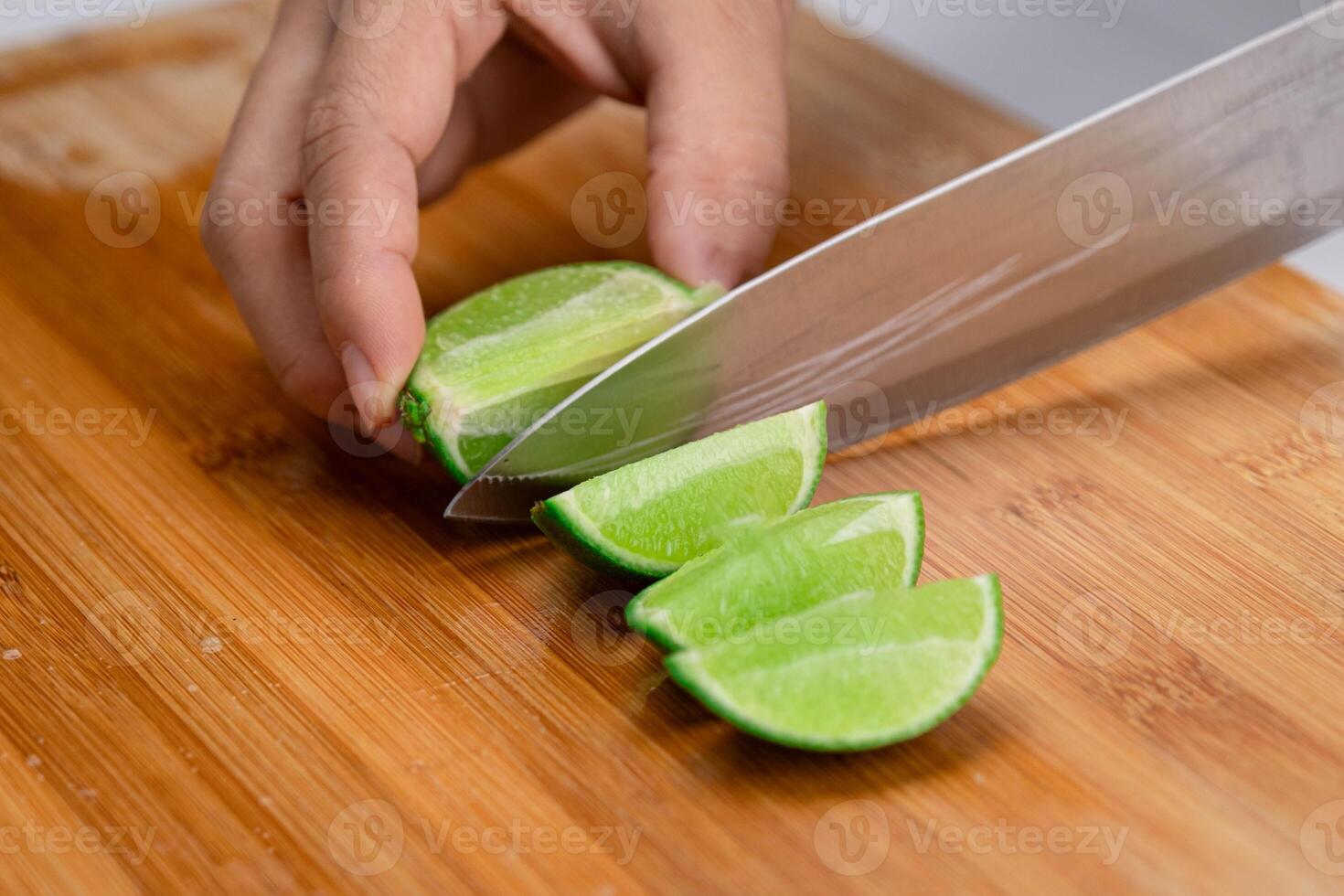 Female hand holding knife is cutting lime on a wooden board in Kitchen. Cutting fresh lemon into pieces close up. Hight Vitamin C Natural photo