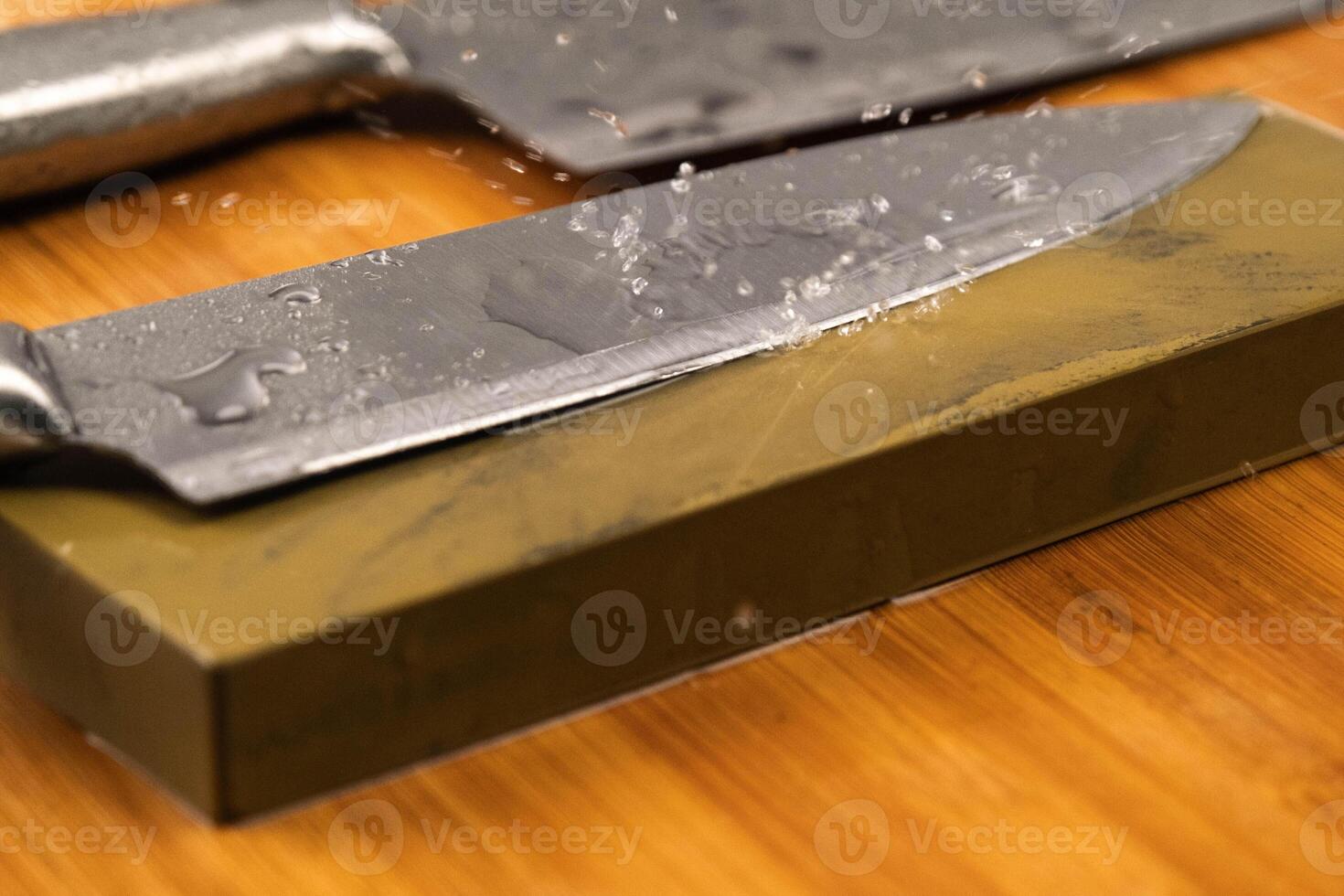 Sharpening knives with a Whetstone. Knife sharpening. Sharp knife and sharpening stone on a wooden cutting board. photo