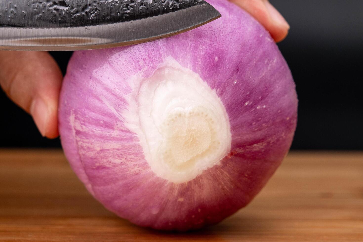 Female hand holding a knife and slicing onions on a wooden cutting board. Cutting big shallots  close up. photo