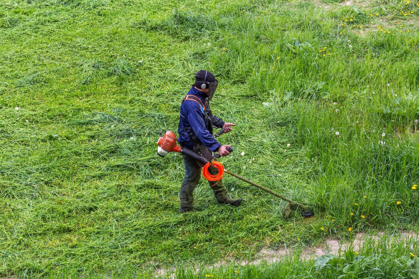 lawnmower man with string trimmer trimming grass at sunny day photo