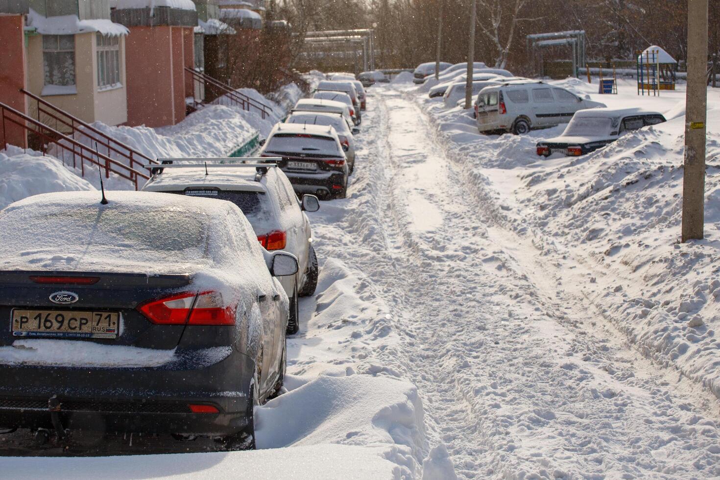 row of snow drifted cars in a row along the street near residential building at winter day snowfall photo