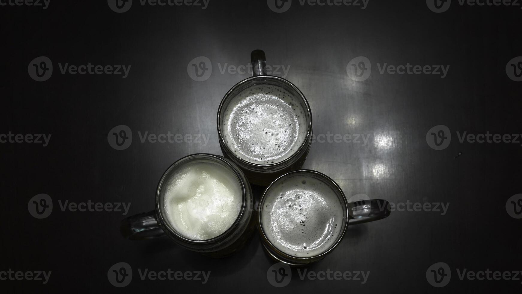 Cheers. Top view of people holding mugs with beer. Top down shot of three pint sized beer mugs on a wooden pub table. Close-up partial view of young friends clinking beer glasses. photo