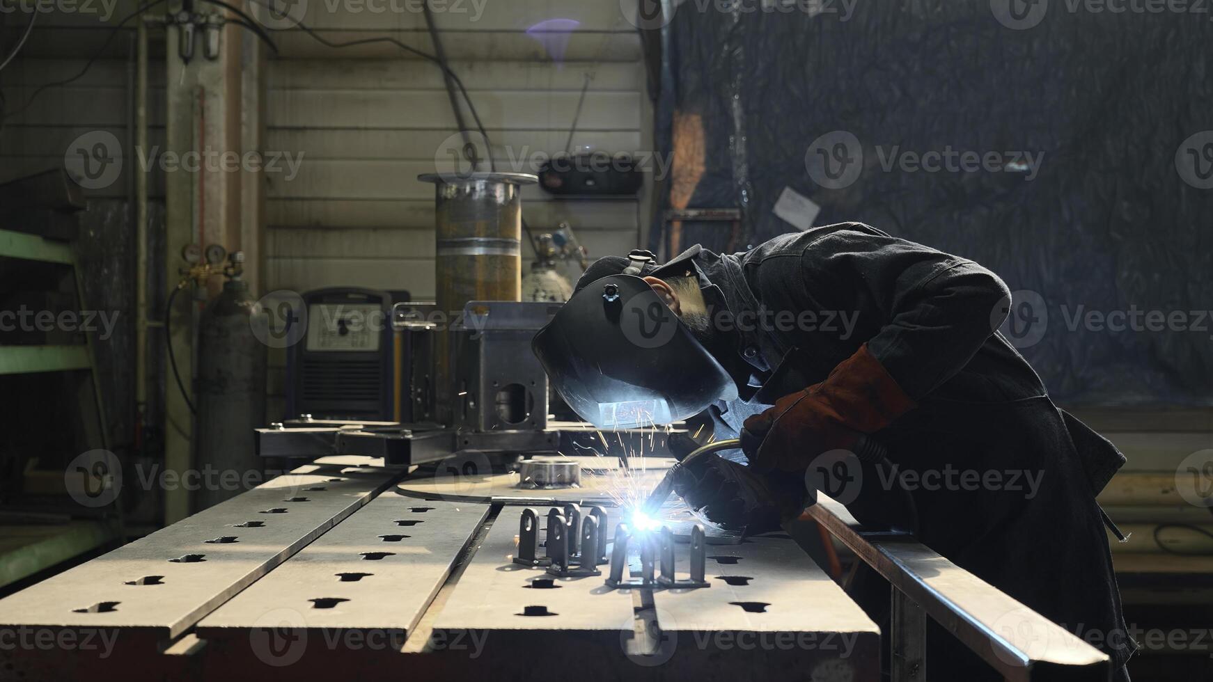 Professional heavy industry worker welder in protective mask and suit works with metal construction on factory. Creative. Steel and iron welding construction site, welding machine with sparks and photo