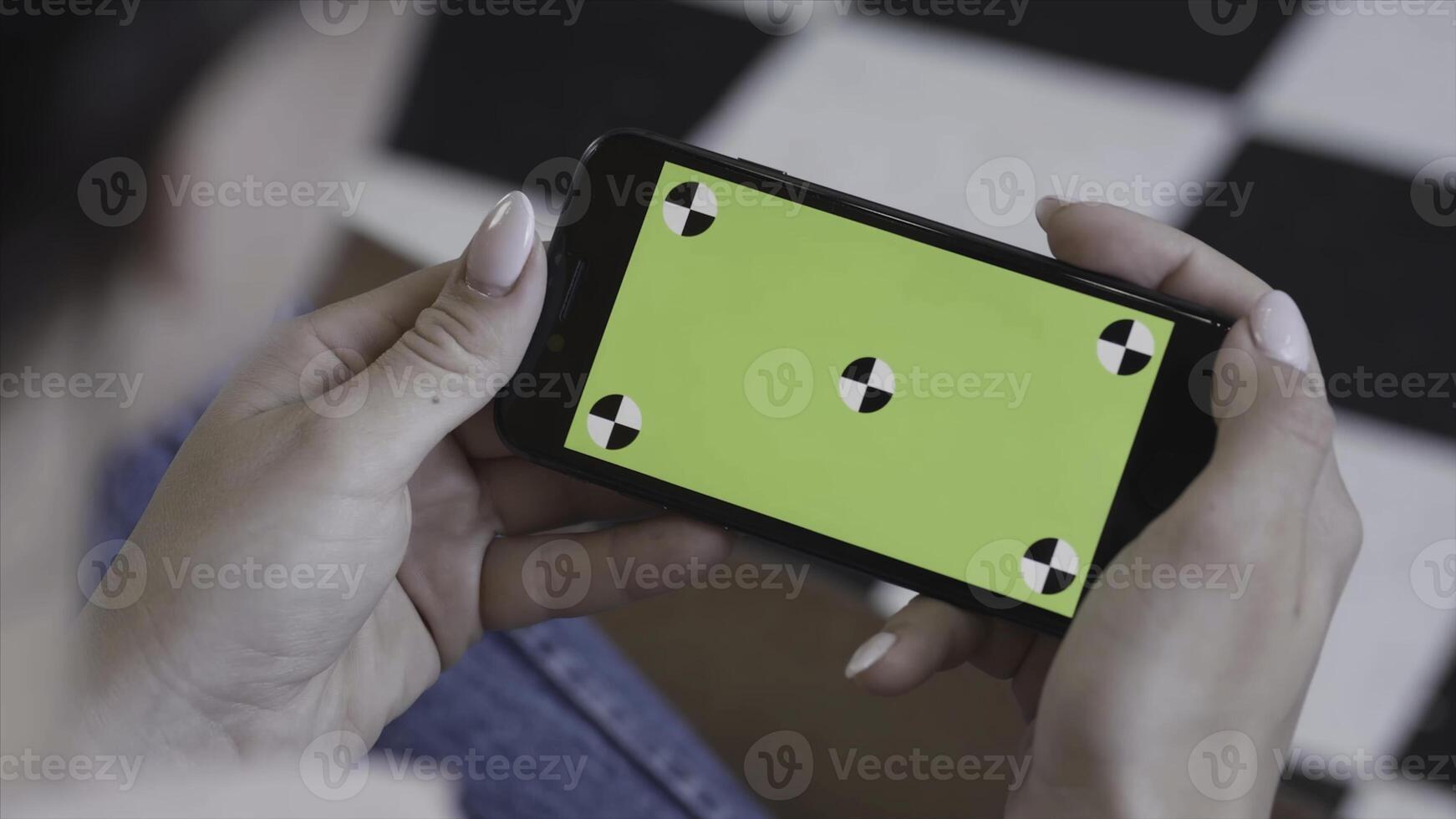Female teen girl with dark hair using smartphone with green screen, sitting indoors. Stock footage. Woman holding Iphone with chroma key in horizontal position. photo
