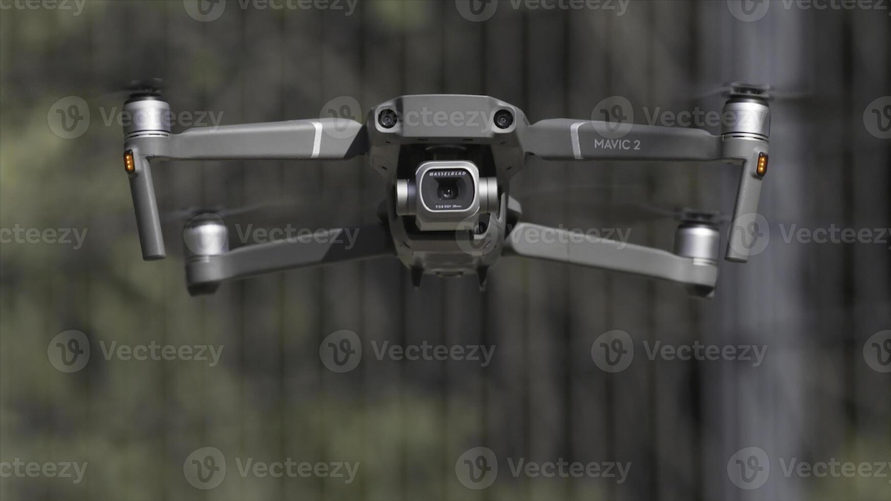 Drone with a camera hovers in the air. Action. Close up of an aircraft and blades that rotate in slow motion on blurred background of green trees, shooting process. photo