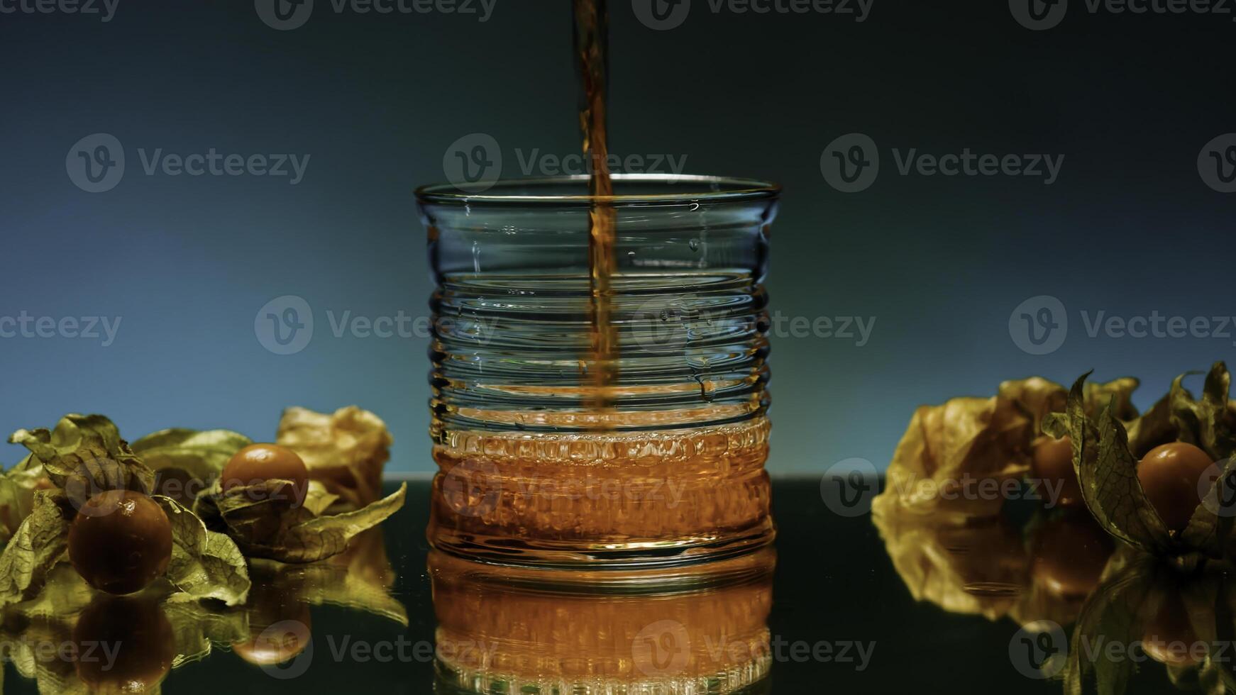 Close up of pouring fruit drink inside an empty glass. Stock clip. Bar counter decorated by small yellow berries on the background of a wall with changing lights. photo