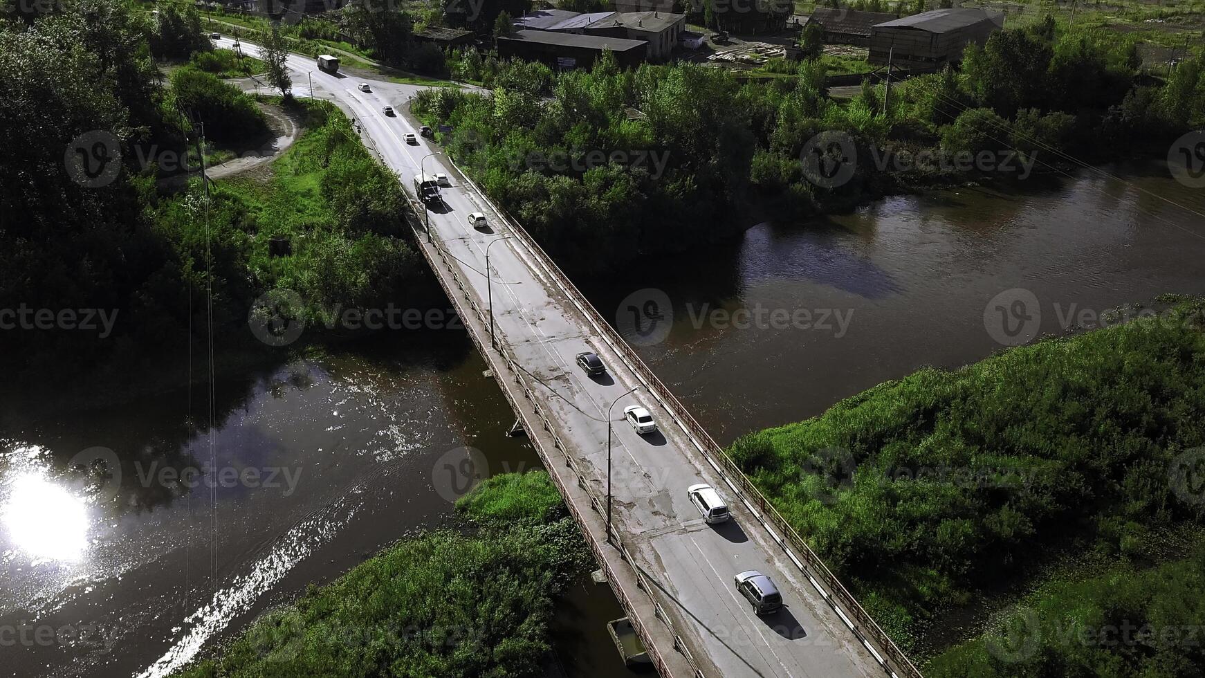 Aerial view of a river and a bridge with driving cars on a summer day. Clip. Summer village surrounded by green vegetation. photo