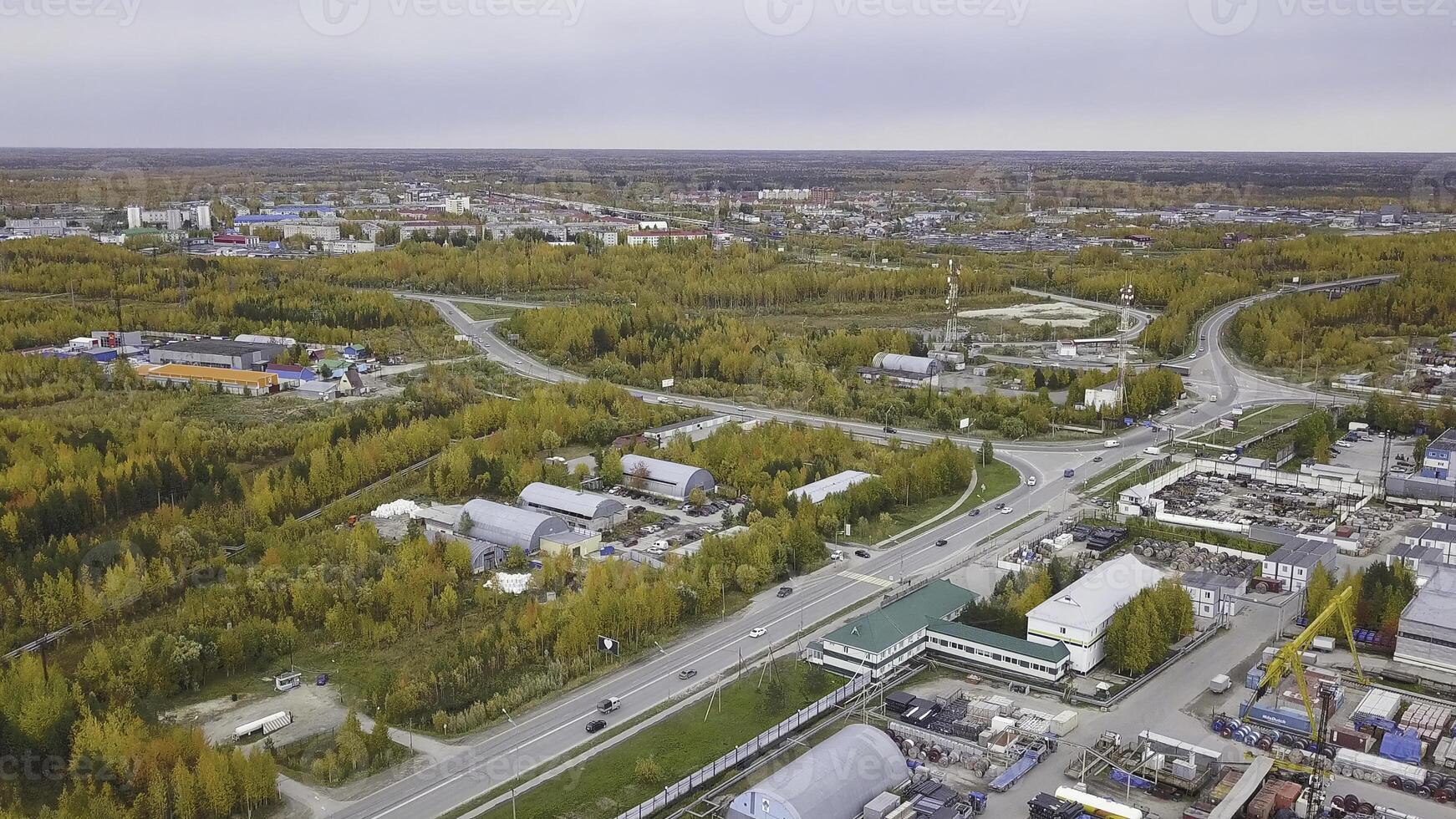 Aerial top view of beautiful autumn trees and the industrial area of the city with buildings. Clip. Many moving cars on the roads of a city surrounded by yellow trees. photo