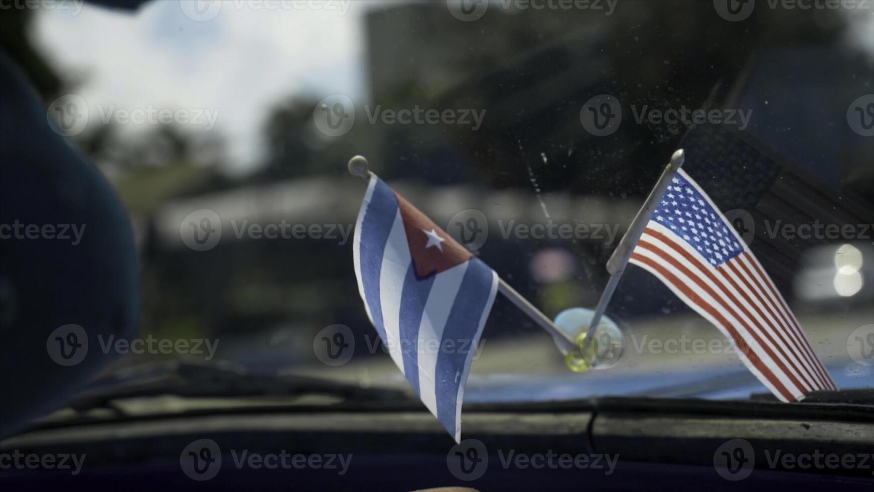 Close-up of flags of America and Cuba in car. Action. Beautiful flags adorn panel of retro car on background of road in hot country. Decoration for car photo