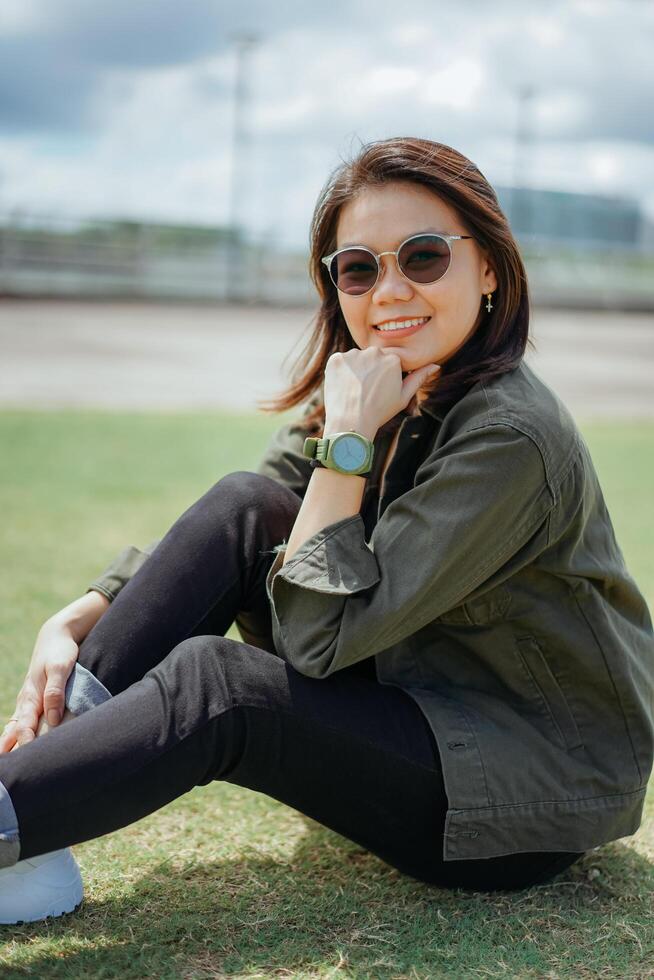 joven hermosa asiático mujer vistiendo chaqueta y negro pantalones posando al aire libre foto