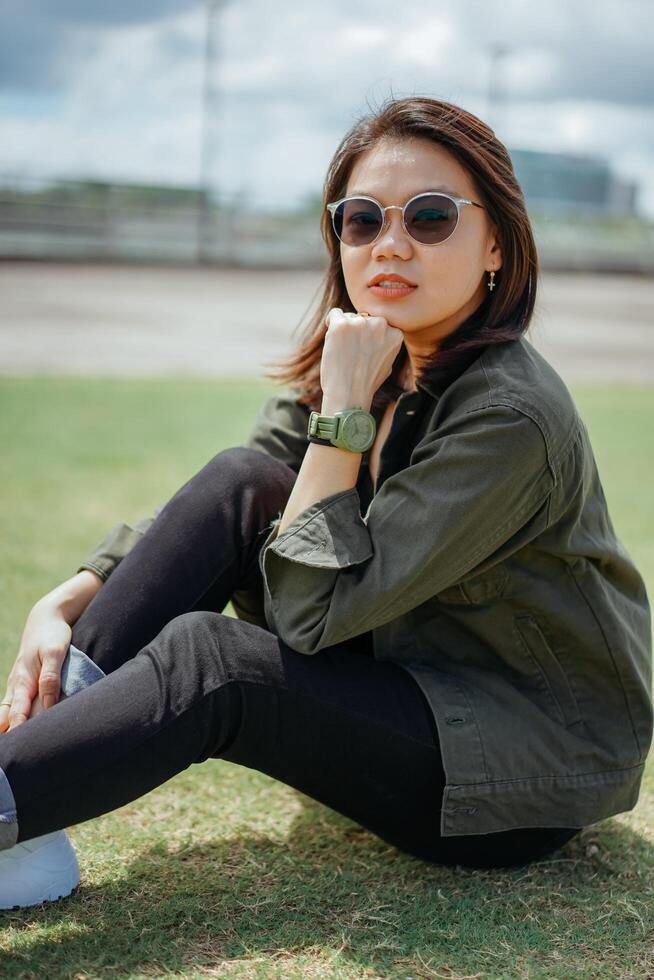 joven hermosa asiático mujer vistiendo chaqueta y negro pantalones posando al aire libre foto