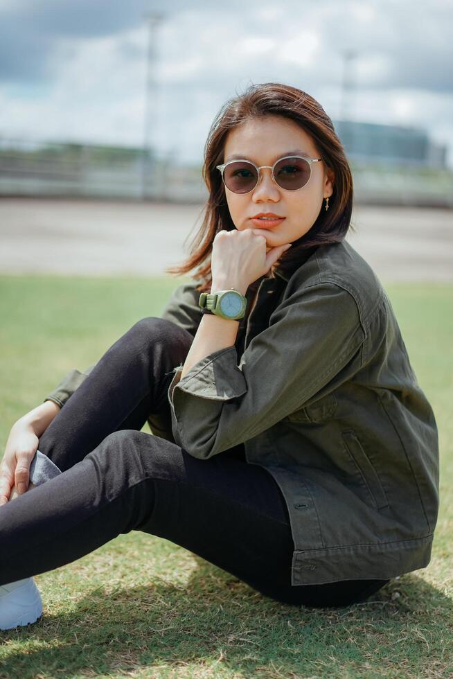 joven hermosa asiático mujer vistiendo chaqueta y negro pantalones posando al aire libre foto