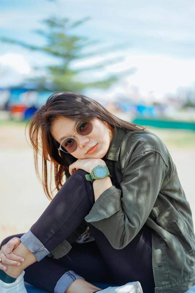 jugando ukelele de joven hermosa asiático mujer vistiendo chaqueta y negro pantalones posando al aire libre foto