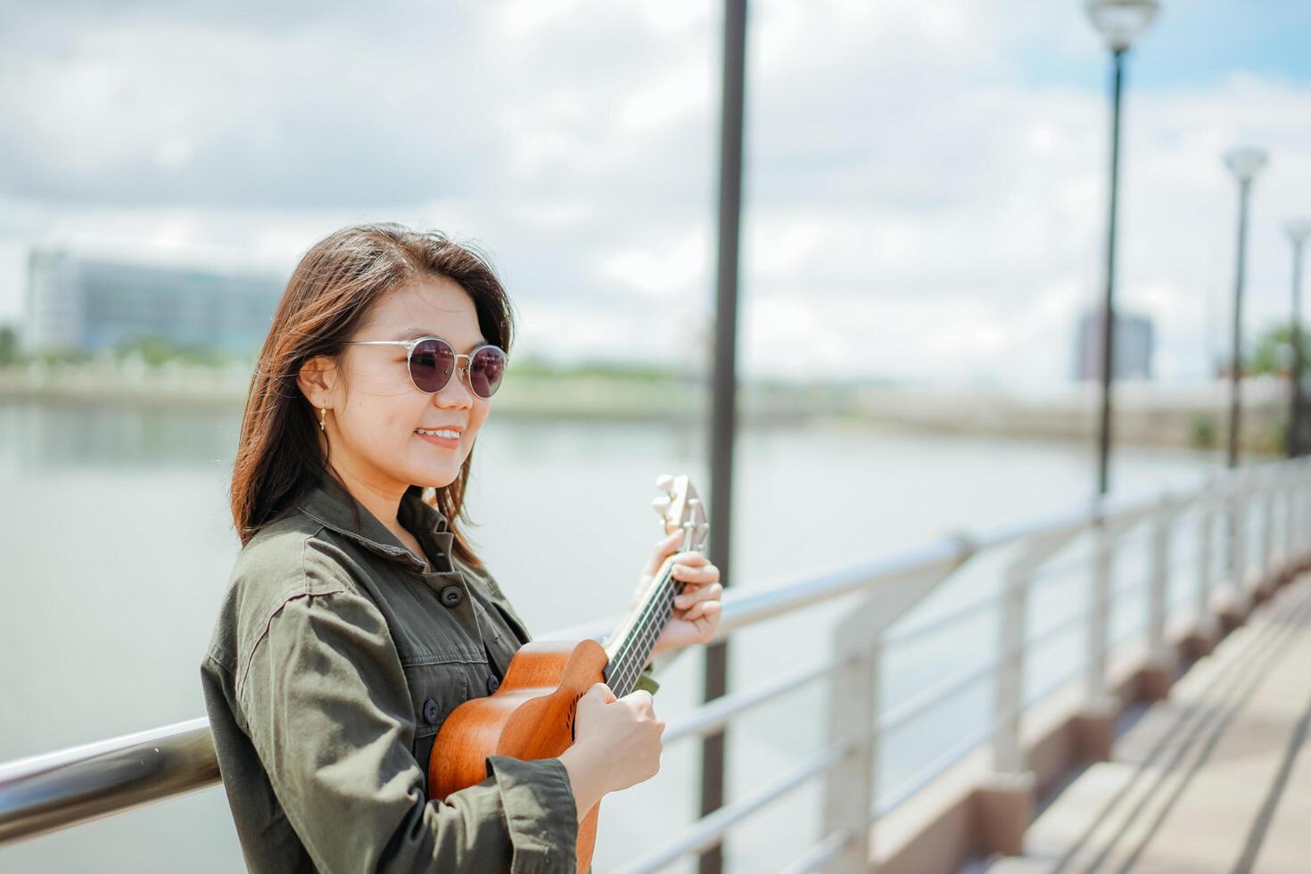 Playing Ukulele of Young Beautiful Asian Woman Wearing Jacket And Black Jeans Posing Outdoors photo