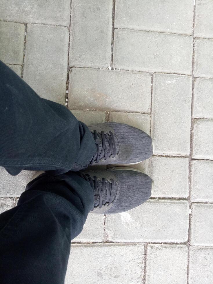 a pair of black shoes on brick paving, wearing black trousers, photographed from above photo