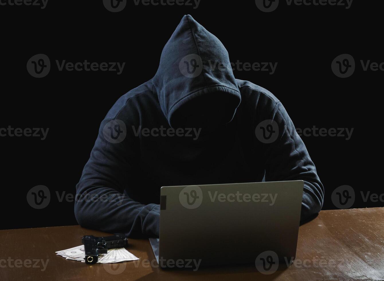 Portrait hacker spy man one person in black hoodie sitting on table looking computer laptop used login password attack security to data digital internet network system night dark background copy space photo