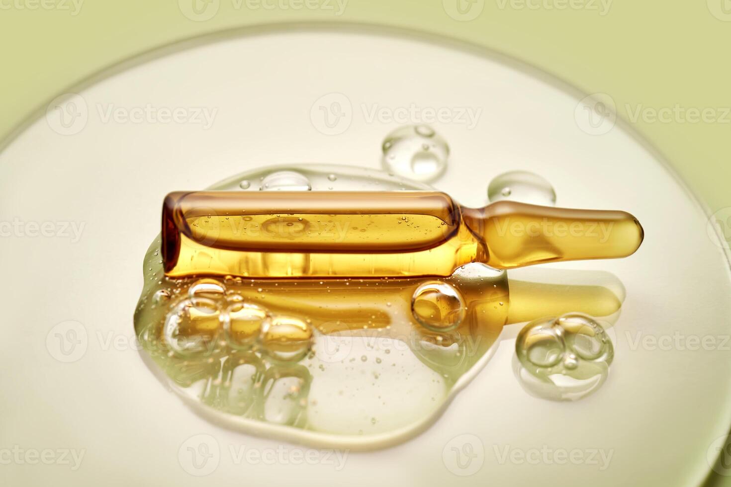 Ampoule in a drop of cosmetic gel on a green background. photo