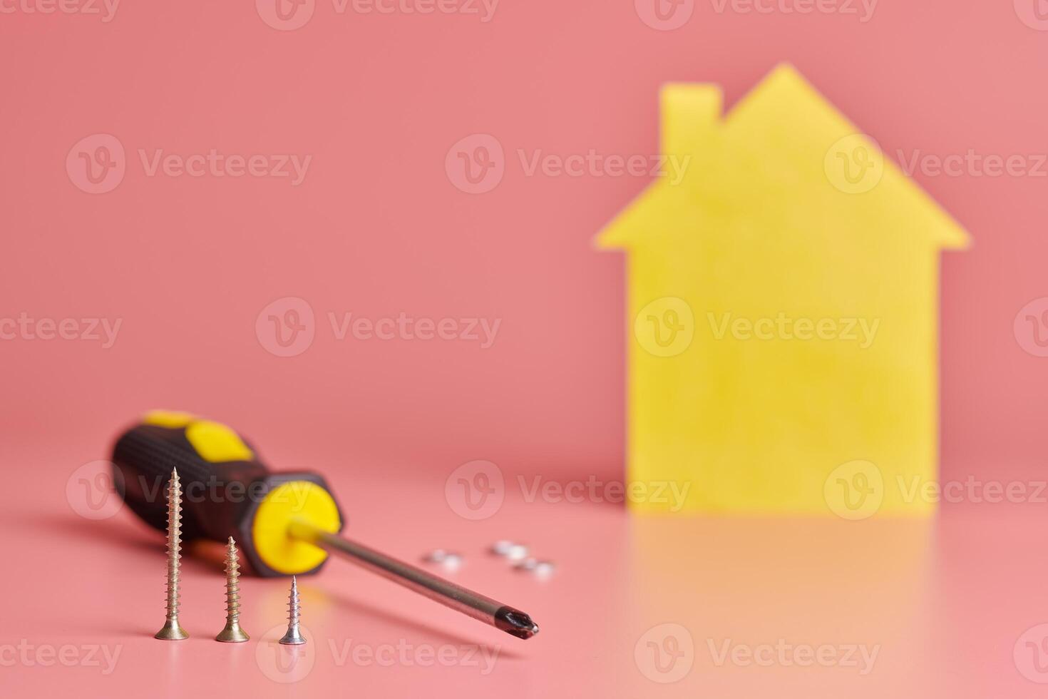 Home repair and redecorated concept. House renovation. Screws and yellow house shaped figure on pink background. photo