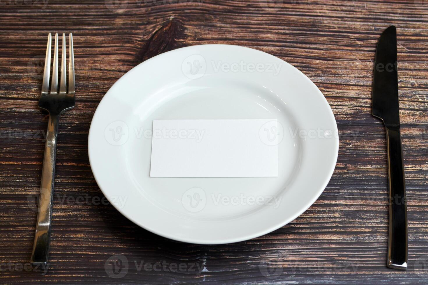 vacío plato en mesa con cuchillería y blanco negocio tarjeta, parte superior vista. mensaje para visitante de restaurante o cafetería. negocio almuerzo sin consejos concepto. foto