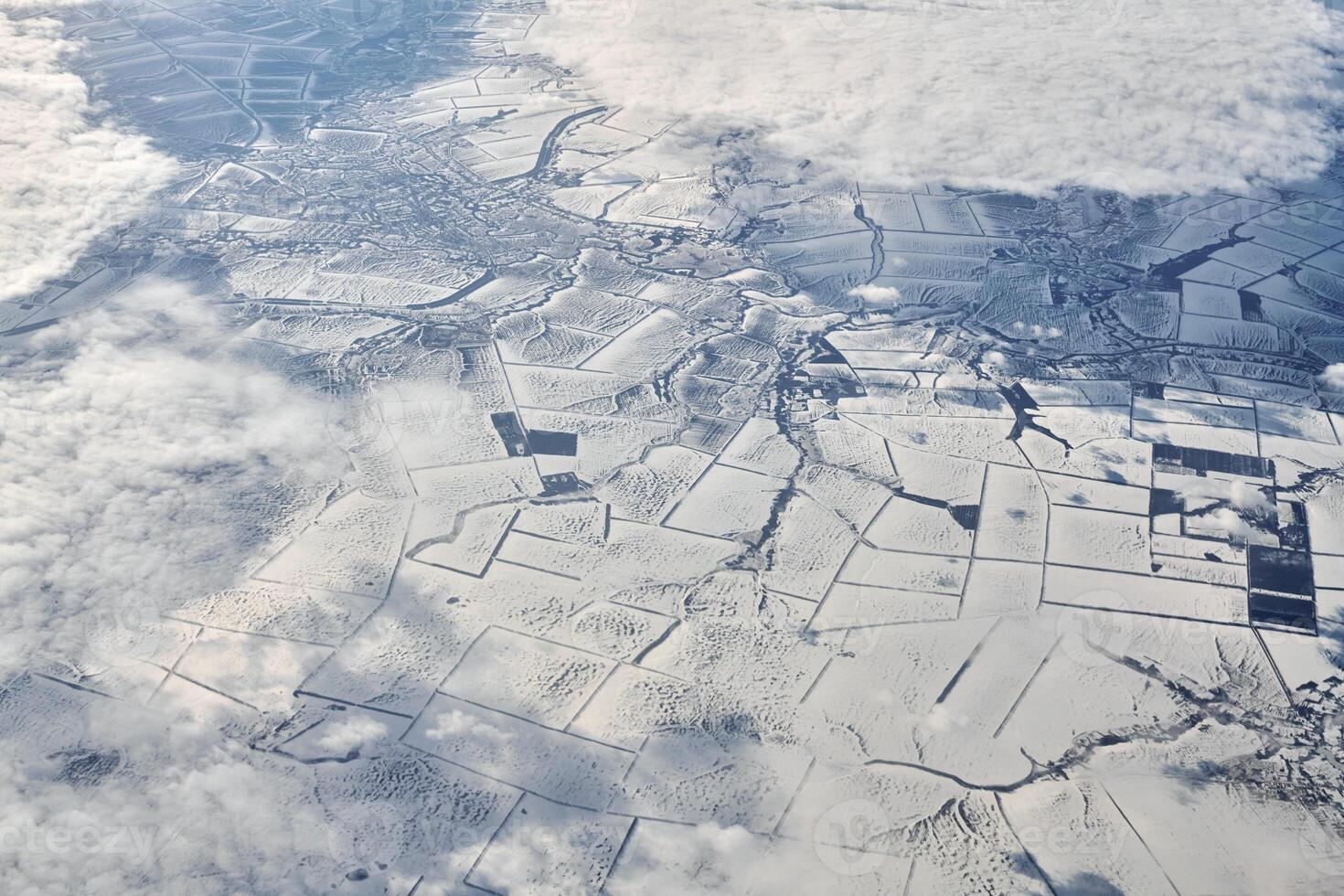 Aerial view over clouds top to snow covered rivers, fields and roads, winter fresh frosty air photo