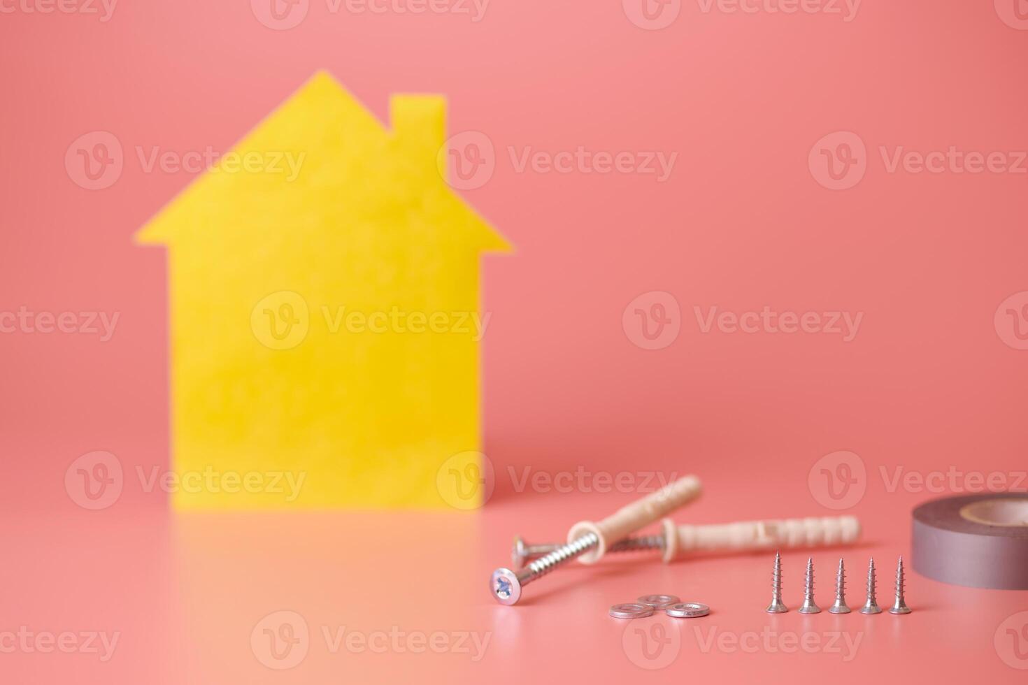 House renovation concept. Home repair and redecorated. Screws and yellow house shaped figure on pink background. photo
