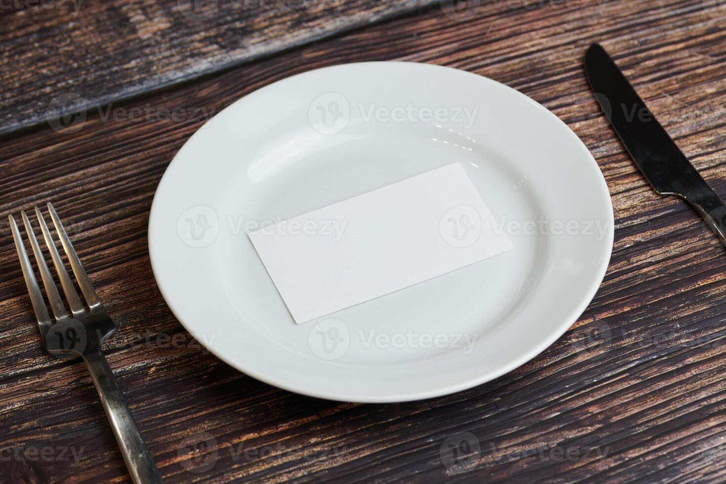 Empty plate on table with cutlery and blank business card, top view. Message for visitor of restaurant or cafe. Business lunch without tips concept. photo