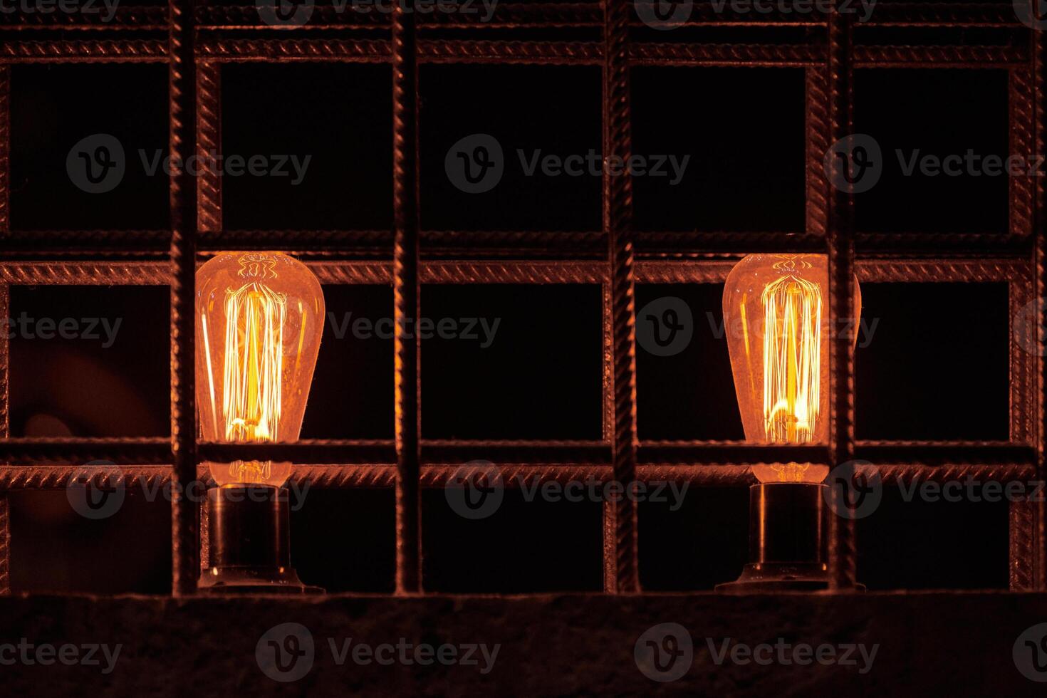 Two decorative incandescent light bulbs inside loft partition from reinforced steel bar photo