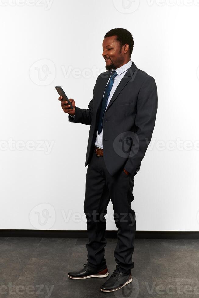 un hombre negro afroamericano sonriente con traje de negocios se ve en el fondo de la pared blanca del teléfono inteligente foto