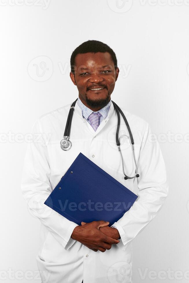 Smiling black bearded doctor man in white robe holds medical clipboard, isolated on white background photo