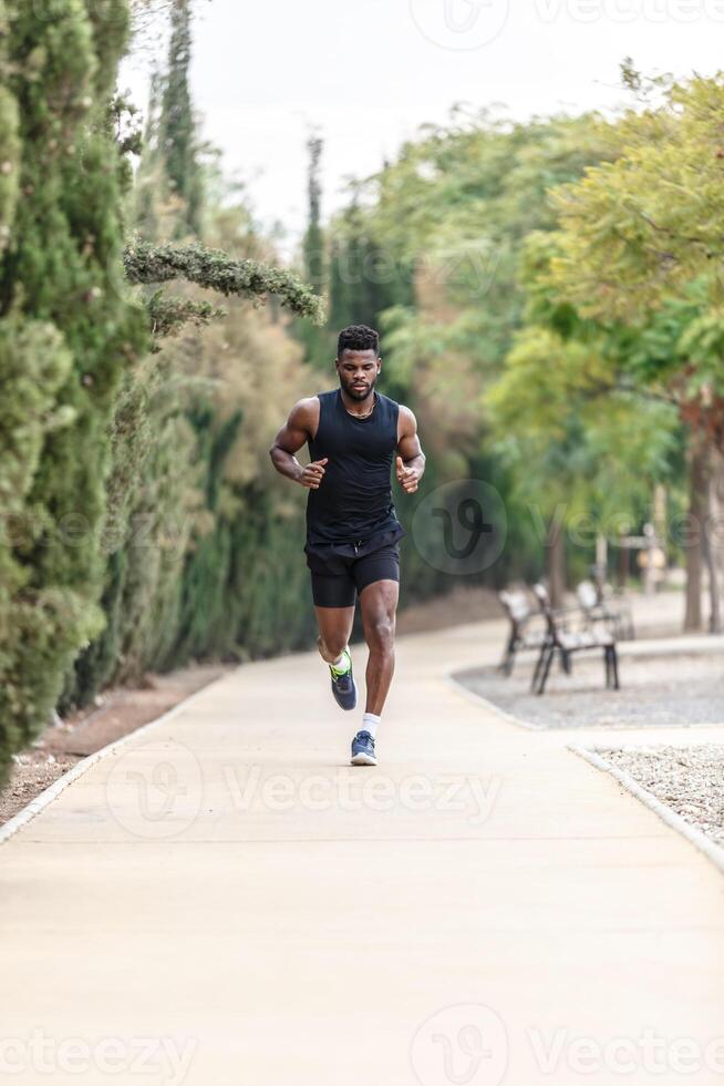 African American sportsman in activewear jogging along park during morning exercise photo