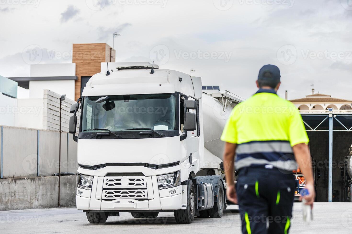 Unrecognizable male worker with parked white tanker truck in factory photo
