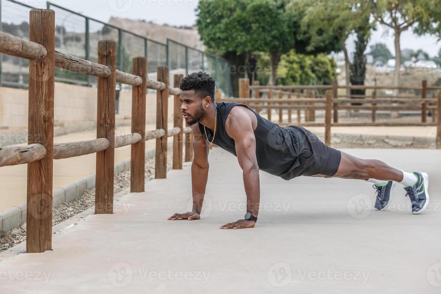 Black sportsman doing plank exercise in park photo