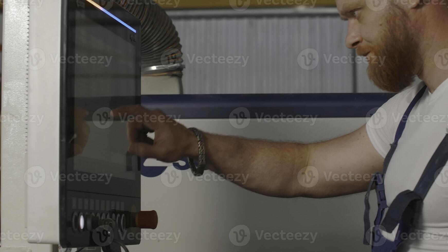 Man clicks on control panel. Creative. Man with beard in work uniform at factory. Man adjusts control panel of industrial machines photo