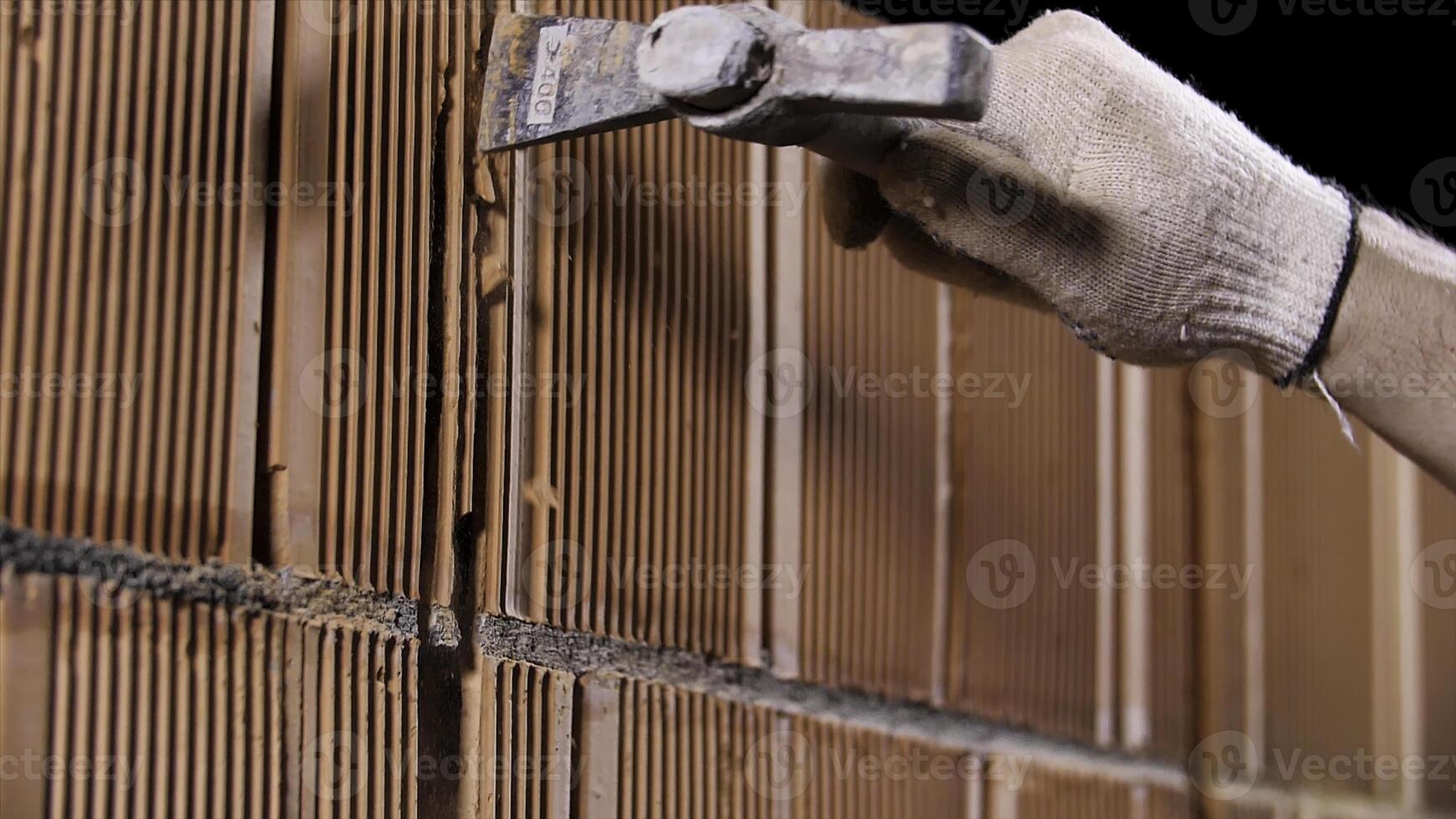 Close up of a man hammering the wall made of ceramic blocks at the construction site. Stock footage. Worker in protective gloves making a hole in the wall. photo