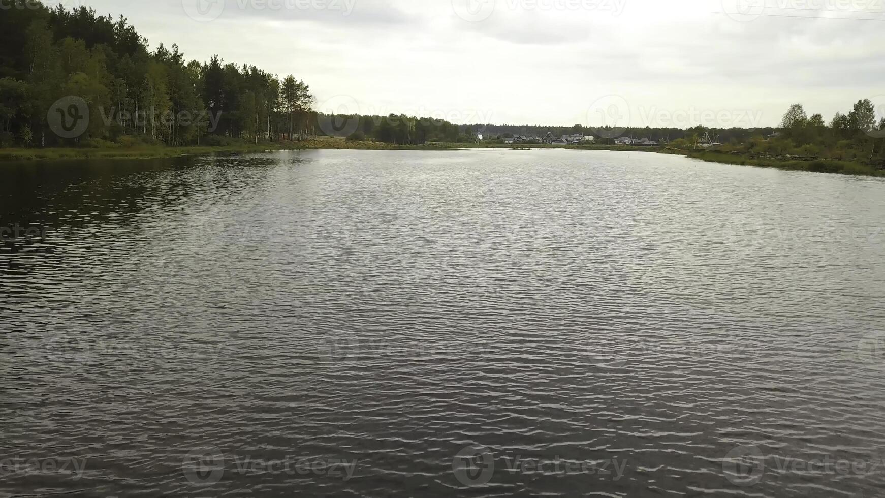 Top view of lake on background of forest shores and village. Stock footage. Beautiful waters of lake reaching village on horizon in summer photo