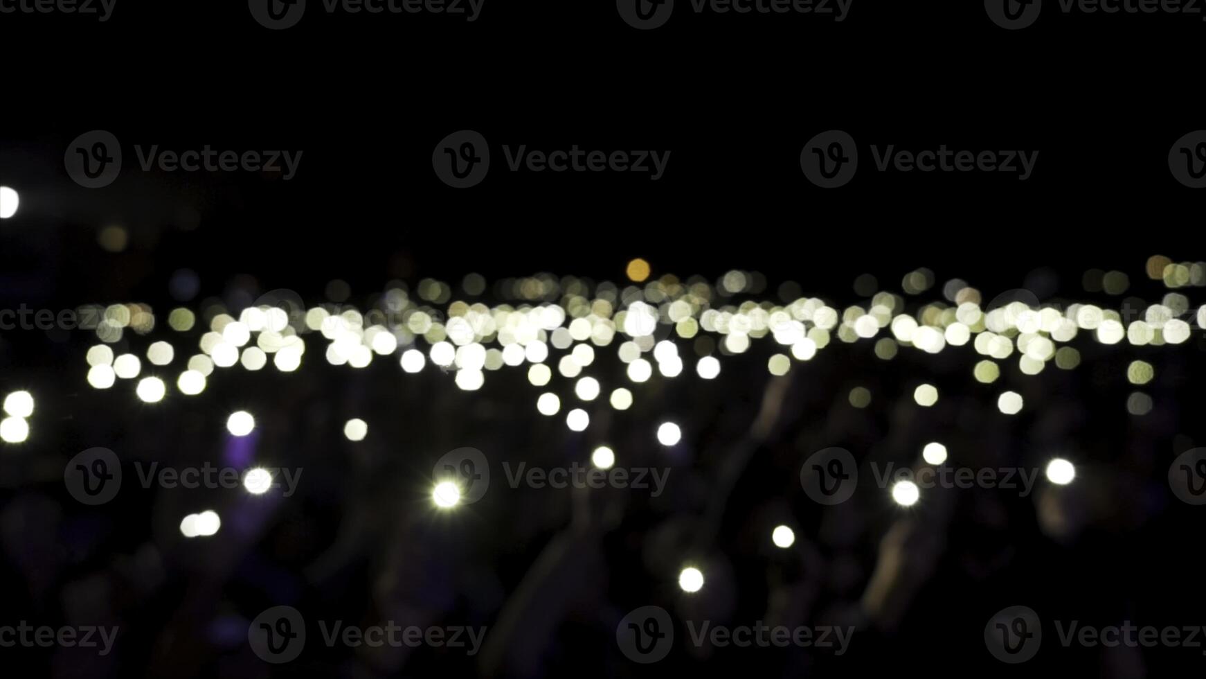 Defocused spectators in hall with lights waving in the dark. Action. Audience holding phones with shining flashlights during the concert, romantic atmosphere. photo