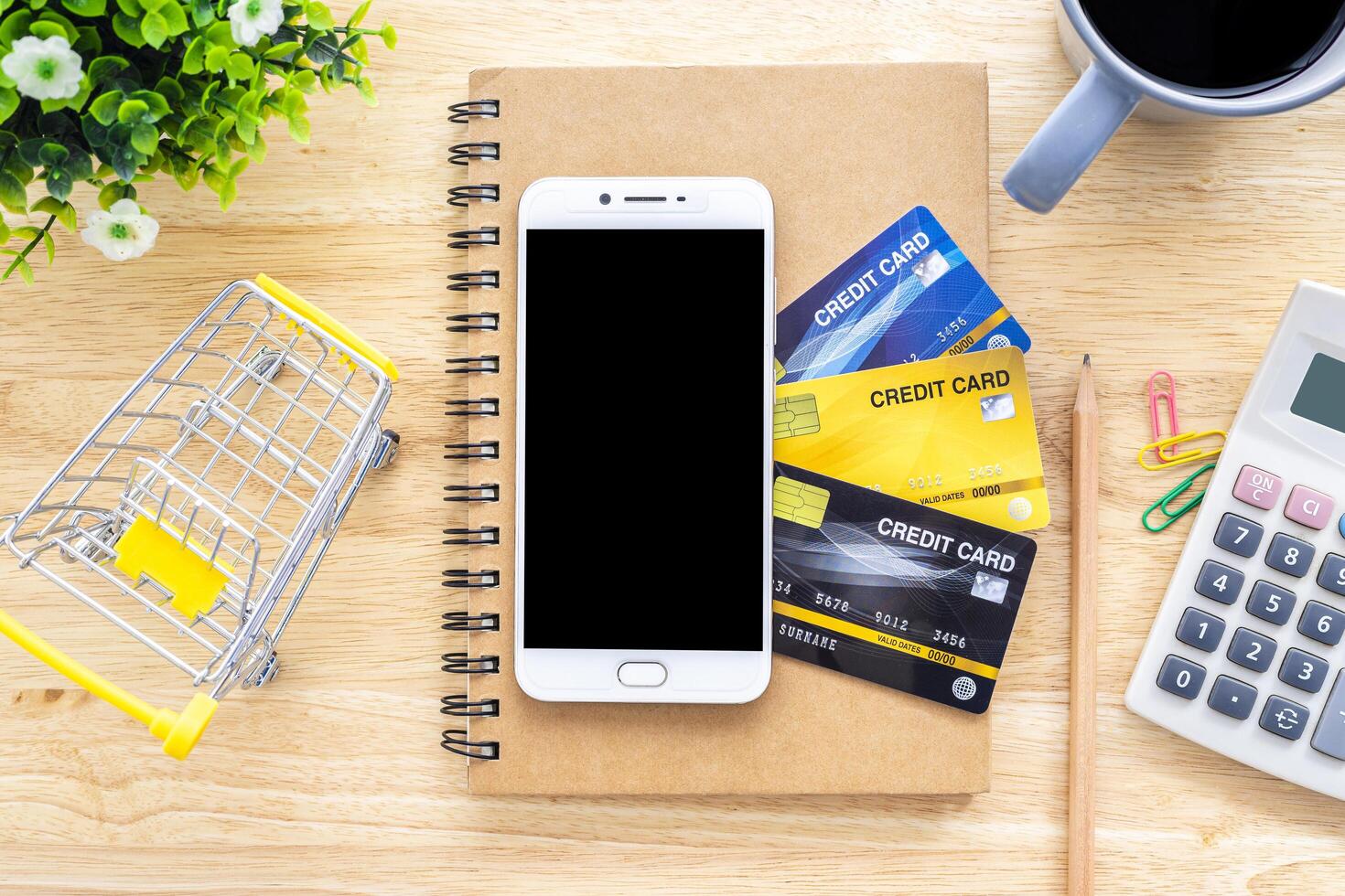 Smartphone on Credit cards,notebook,flower pot tree,Shopping cart,calculator and coffee cup on wooden background,Online banking Concept,Top view office table photo