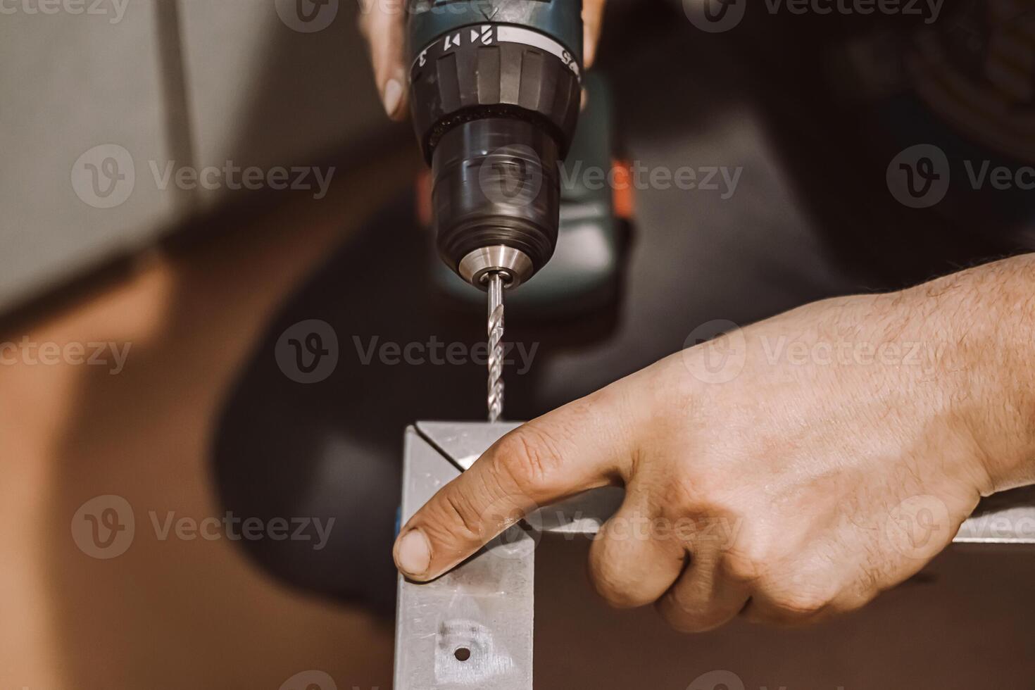 Male mechanic works in workshop with electric drill. Worker drills hole in metal. Lifestyle, professional activity. Hands hold repair tool. photo