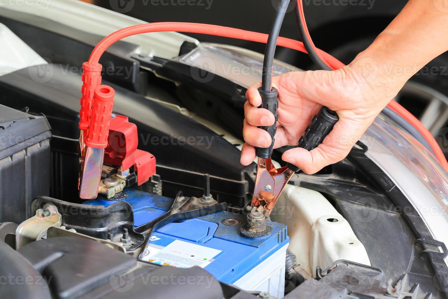 Car mechanic uses battery jumper cables charge a dead battery. photo