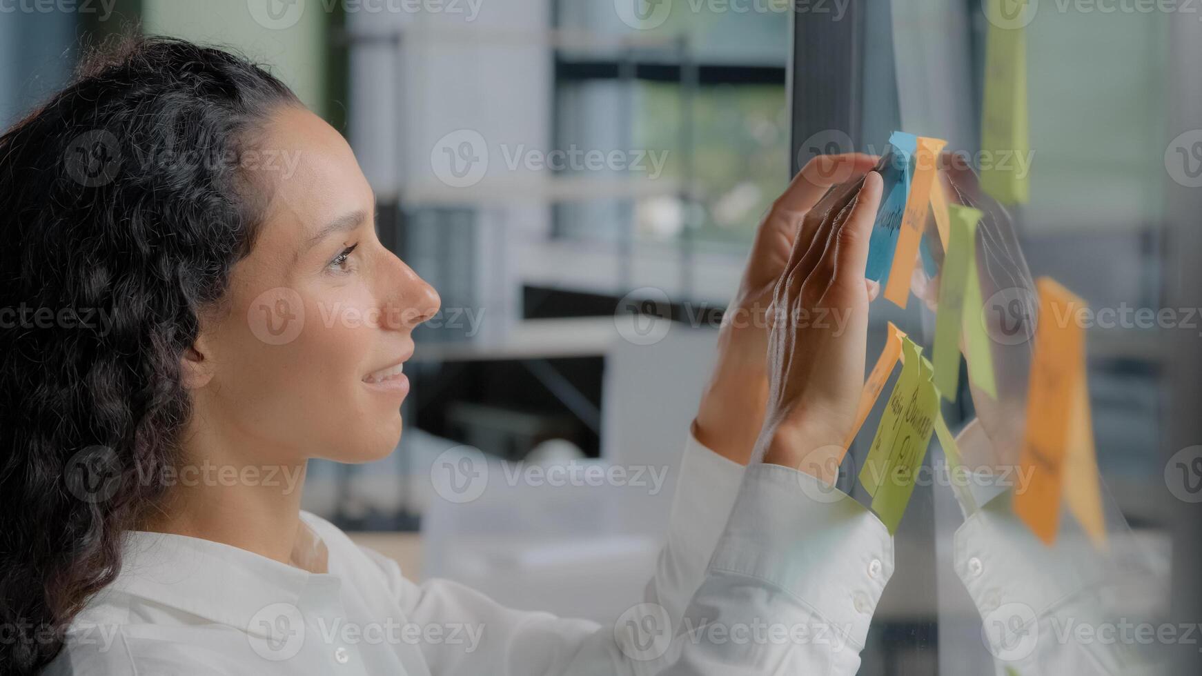 Side view smiling happy successful businesswoman taking notes on stickers writing reminders on color sticky label joyful female project manager developing startup strategy creates plan on glass board photo