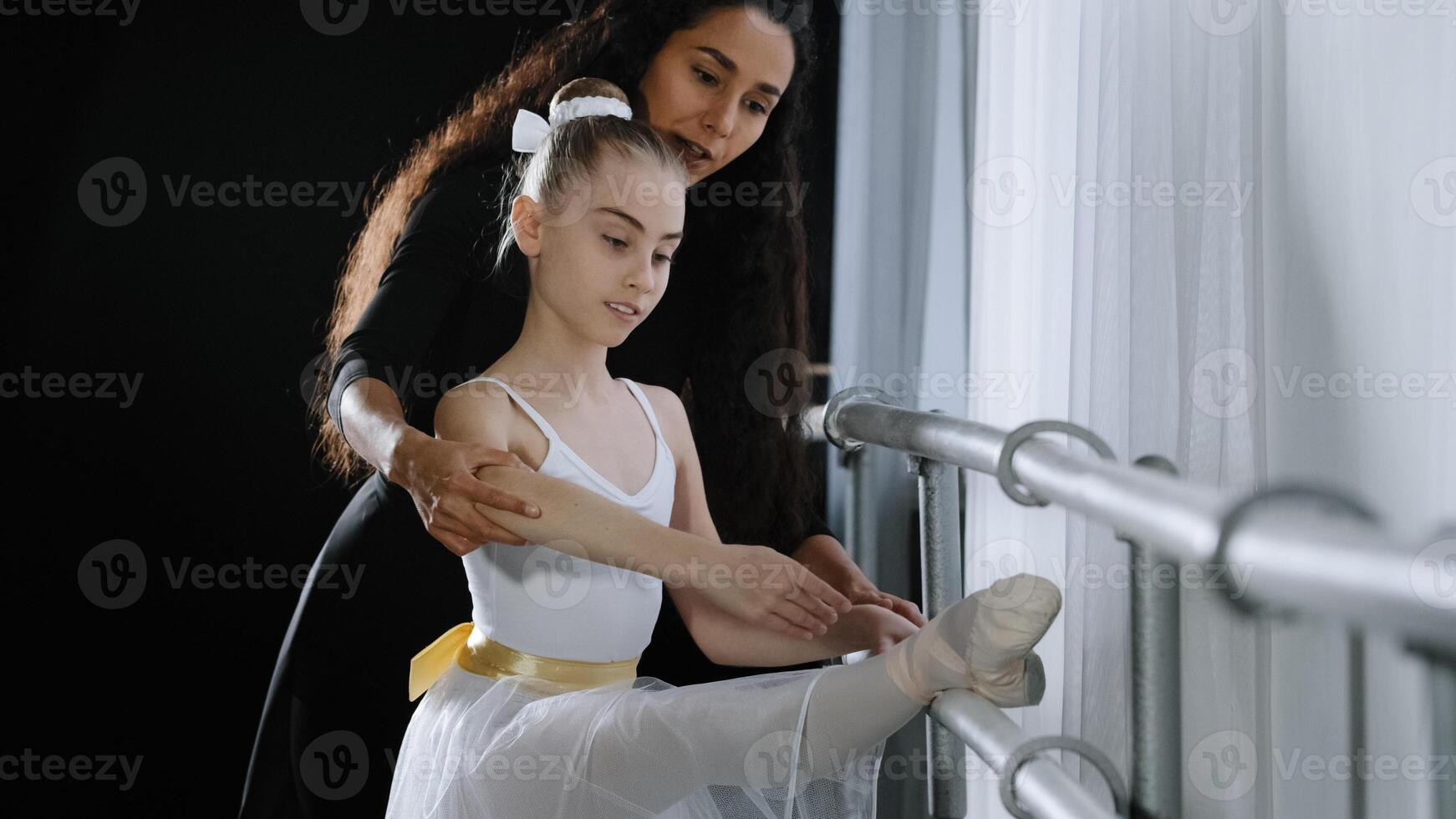 Female choreographer teacher mentor trainer of classical dance teaches posture help with stretching to young student learn dancing teen girl ballerina near ballet barre. Teaching gymnastics class photo