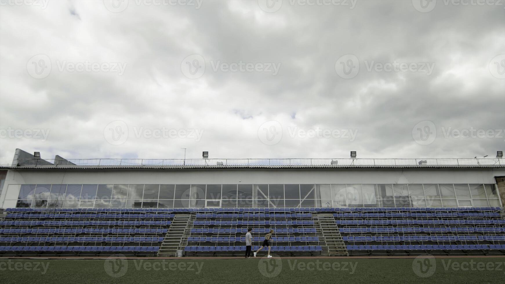 Sports field with training athletes with empty seats and cloudy sky on the background. Stock footage. Concept of olympic games, sport, and active lifestyle. photo