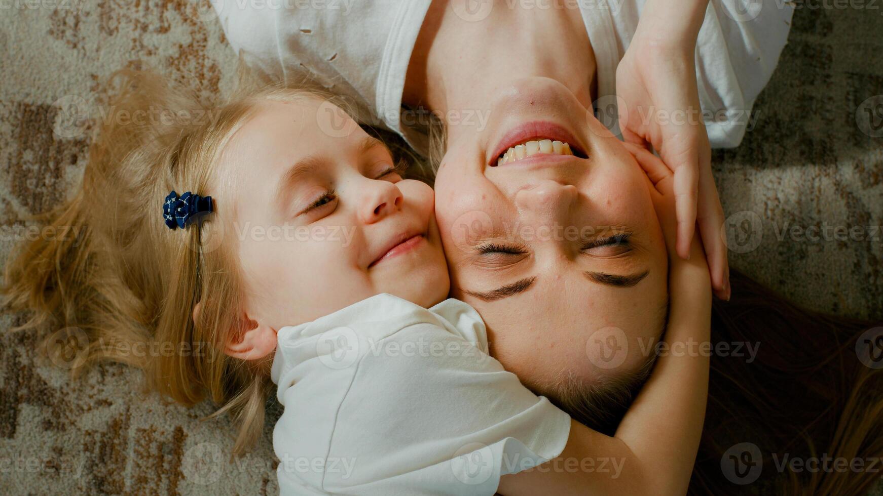 Cute affectionate adopted little kid preschool girl hugging cuddling mother head top view. Child daughter with mum two faces cuddle lying down at home talking smiling with eyes closed tender moment photo