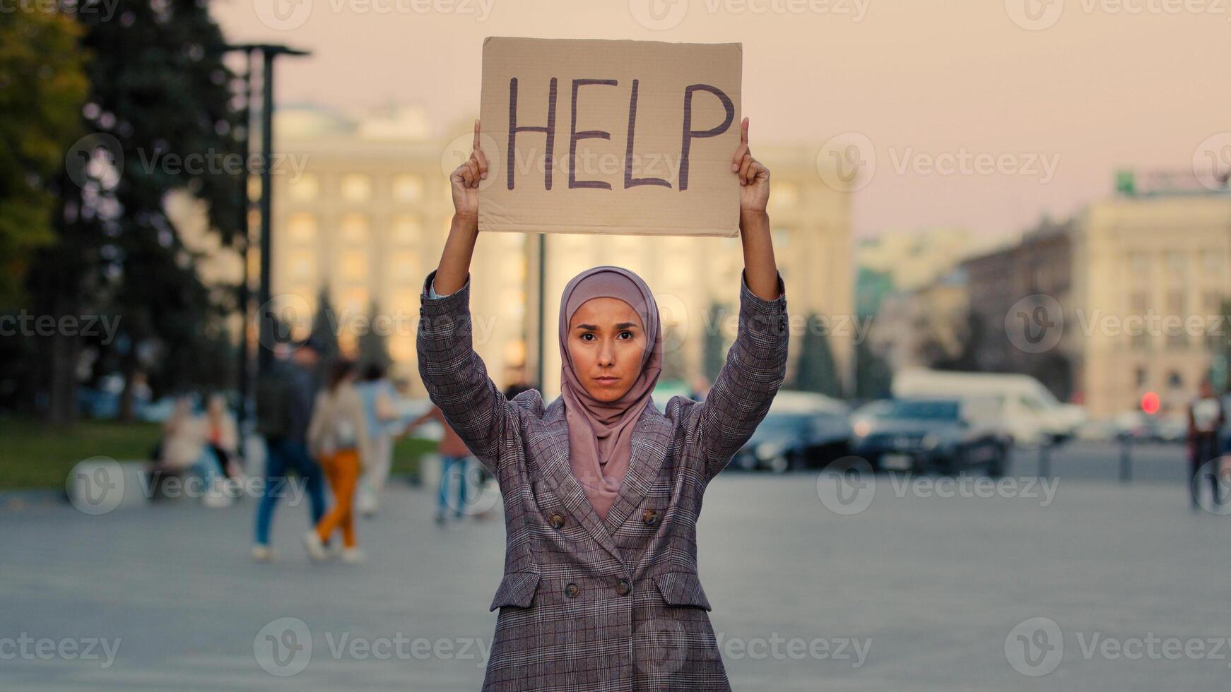 Sad lonely poor muslim girl wears hijab woman stands in city looking at camera demonstrates shows cardboard banner text help needs protection work, unemployment discrimination problem concept photo