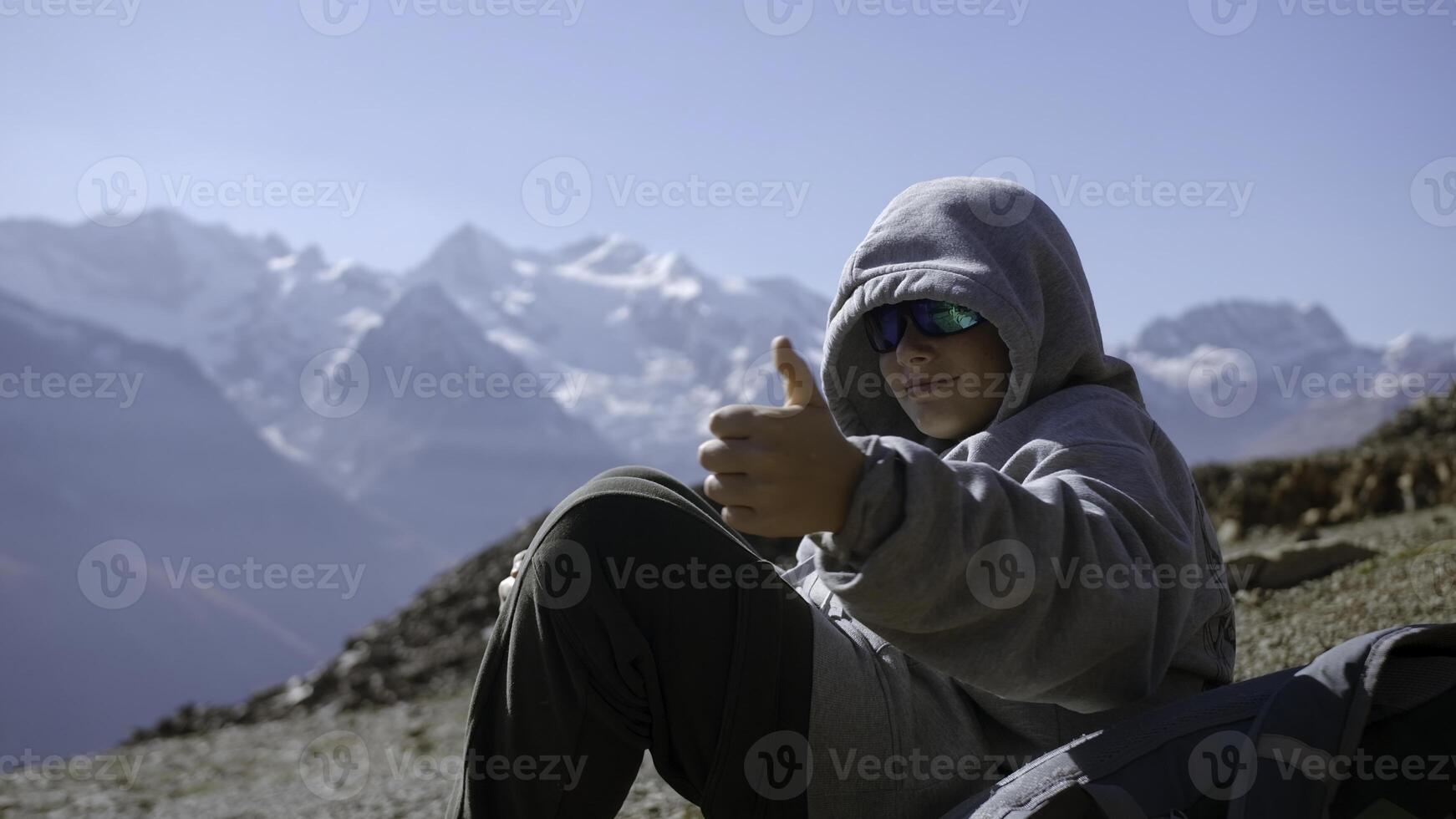 Boy gives thumbs up in mountains. Creative. Boy in ski goggles looks at mountain landscape on sunny day. Beautiful mountain landscape and enjoying boy photo