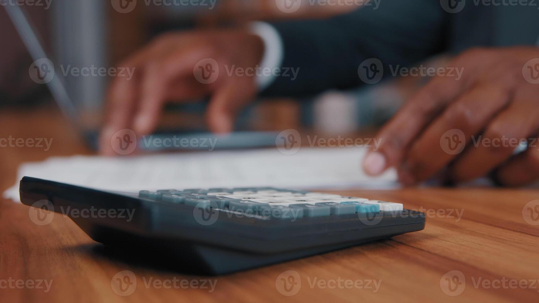 Close-up african american man calculates salary enters data in laptop accountant businessman makes calculation looks for information in paper documents controls business expenses focus on calculator photo